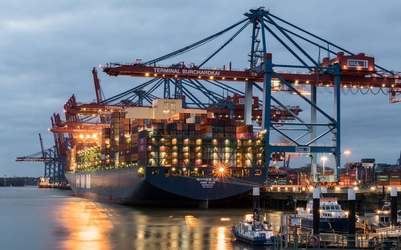 Containerterminal met hijskranen en een containerschip bij avondlicht, beeld bij cybersecurity voor transport en logistiek